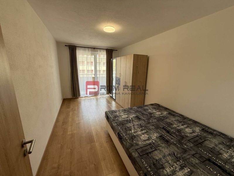 A bedroom in a two-room apartment with a wooden decor floor and a balcony.