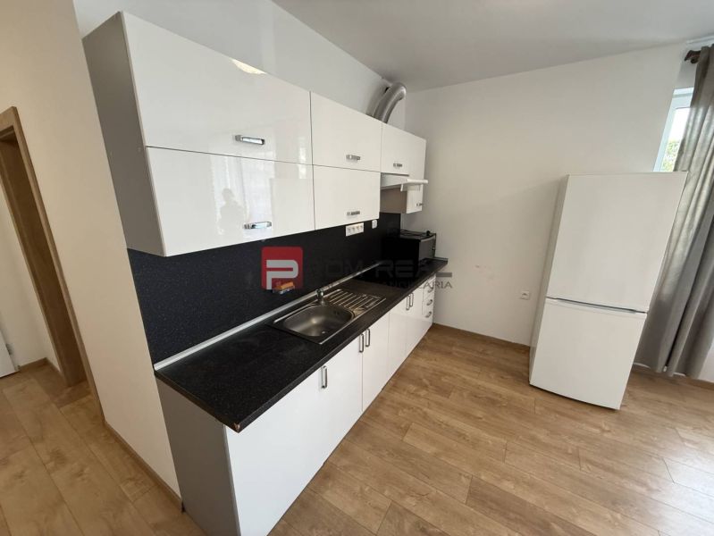A kitchen in a 2-room apartment with a white kitchen unit and a floor with a wooden decor.