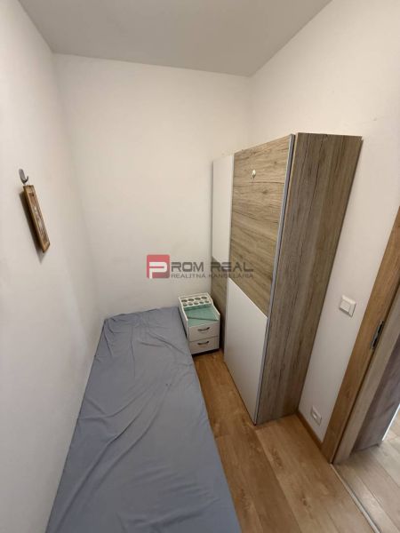 A narrow room with a bed, a wardrobe, and a floor with a wooden decor in a 2-room apartment.