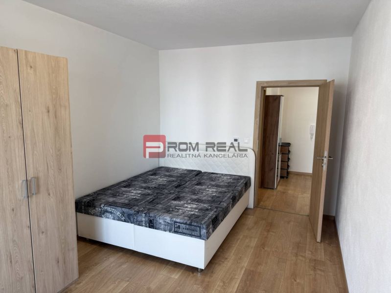 Bedroom in a two-room apartment with wood-decor flooring, a bed, and a wardrobe.