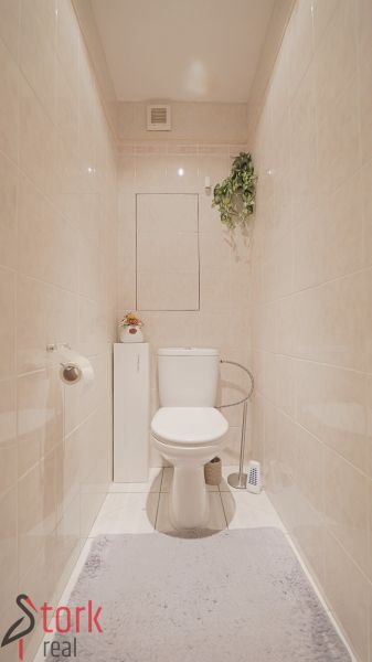 Bathroom with toilet in a 3-room apartment, beige tiles and decorative plants.