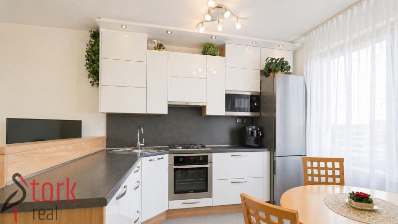 A kitchen in a 3-room apartment with white cabinets, a corner sink, and a dining table.