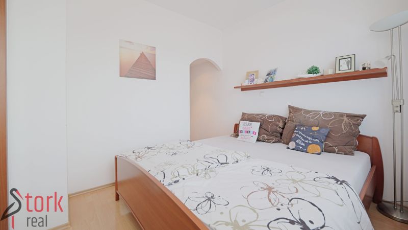 Bedroom in a 3-room apartment with a bed, pillows, and a shelf on white walls.