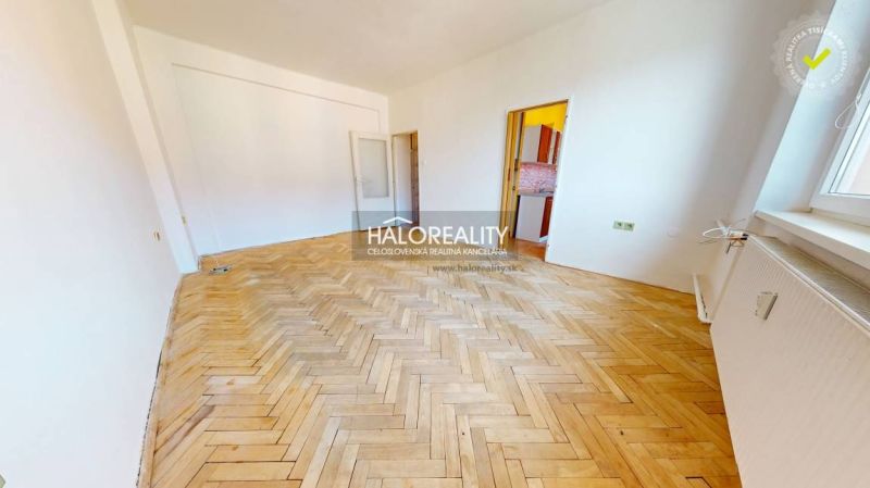 A room in a 2-room apartment with a large floor with wooden decor, white walls, and a window.