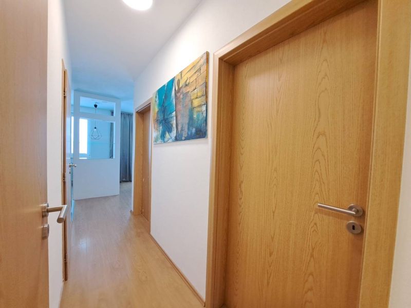 A hallway in a 3-room apartment with a wood-patterned floor and a painting on the wall.