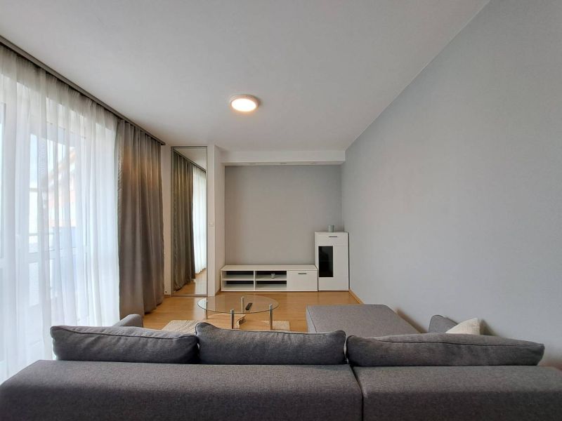 Living room in a three-room apartment with a sofa, glass table, and wooden decor flooring.