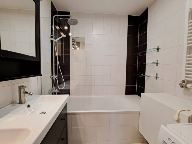 A white bathroom with a bathtub, black tiles, and a shower in a 3-room apartment.