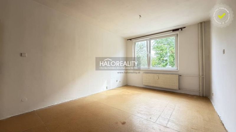 An empty studio apartment with a large window and a wooden-patterned floor.