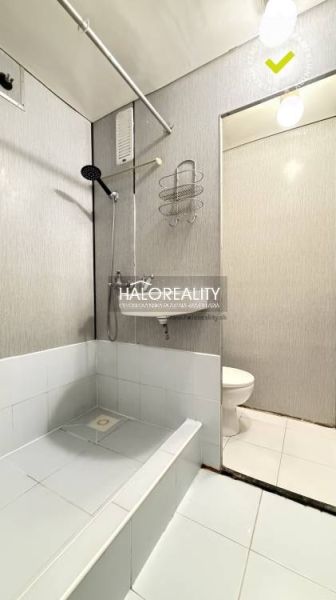 A bathroom in a studio apartment with white tiles and a shower corner.