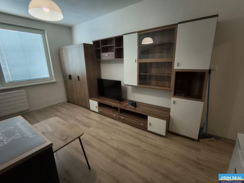 A studio apartment with a wooden floor, cabinets, and a television.