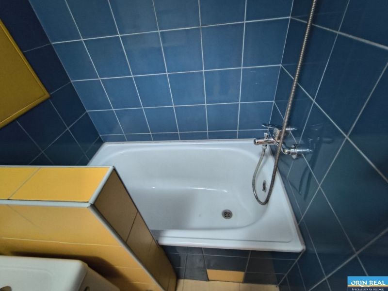 A bathroom with blue and yellow tiles and a bathtub in a studio apartment.