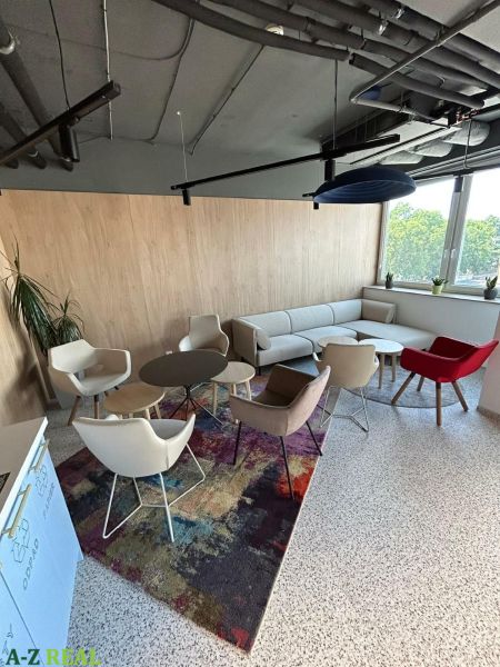 A comfortable office with modern furniture and large windows, carpeted floor.