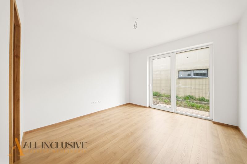 A spacious room with a wood-patterned floor and a large window in a family house.