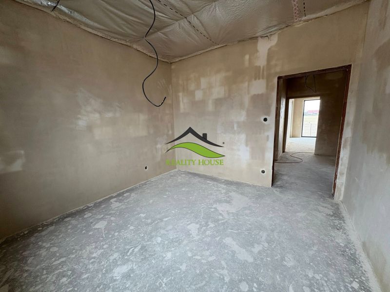 An unfinished interior of a family house with plastered walls and a raw floor.