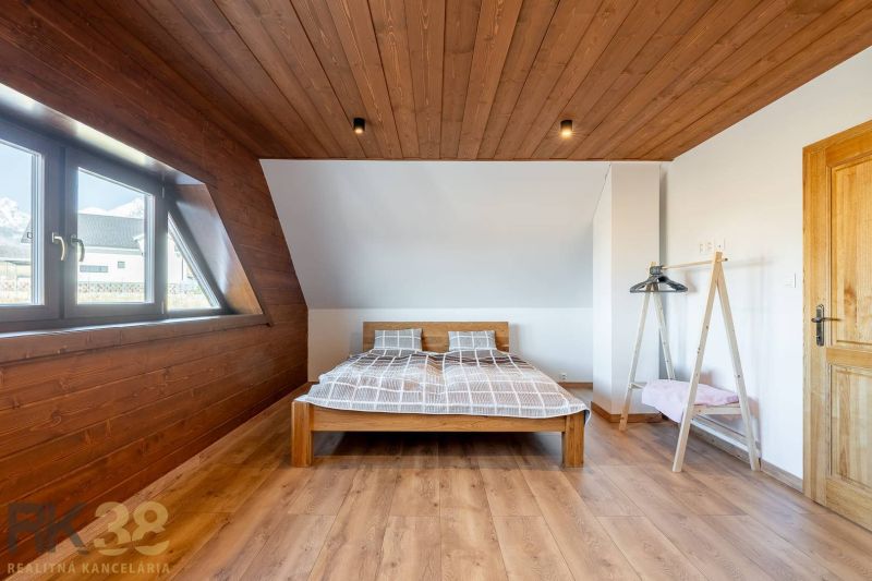 A bedroom in a family house with a bed, a wooden decor floor, and wooden walls.