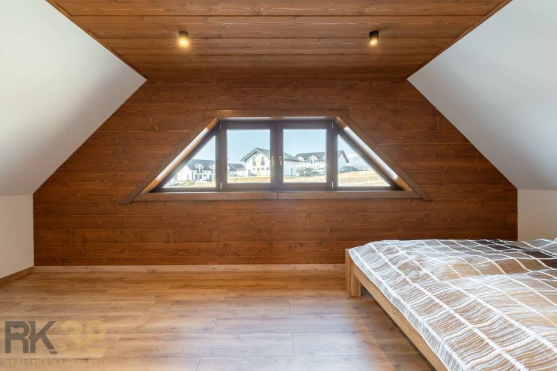 Attic bedroom in a family house with a wooden decor floor and large windows.