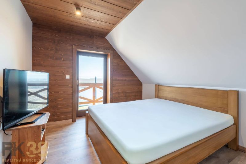 Bedroom of a family house with a bed and a television, floor with wooden decor.
