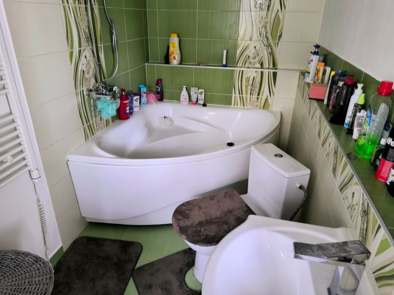 A bathroom in a 3-room apartment with green tiles, a bathtub, and a toilet.