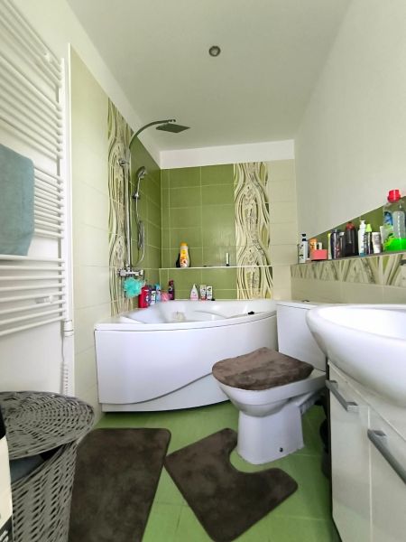 A bathroom in a 3-room apartment with a bathtub, sink, toilet, and green tiles.