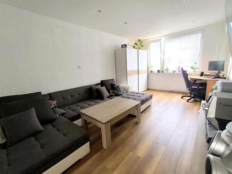 Living room in a three-room apartment with a wooden decor floor, a sofa, and a table.