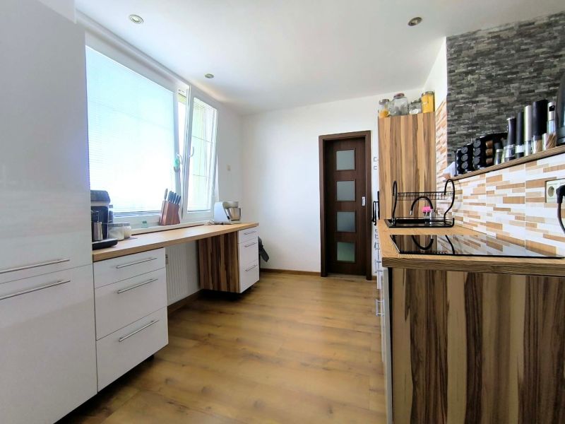A kitchen in a 3-room apartment with a wooden decor floor, light cabinetry, and practical storage spaces.