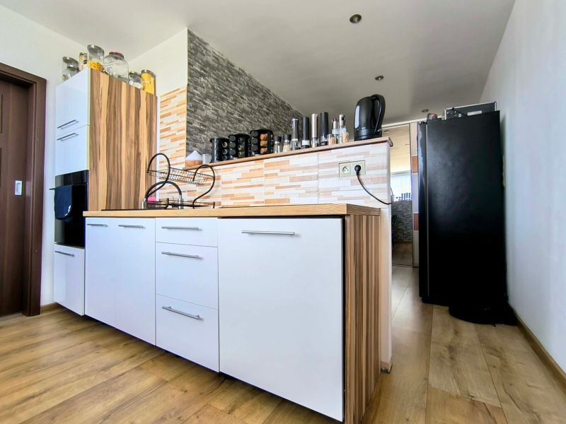 The kitchen of a 3-room apartment with white cabinets, wooden decor, and modern equipment.