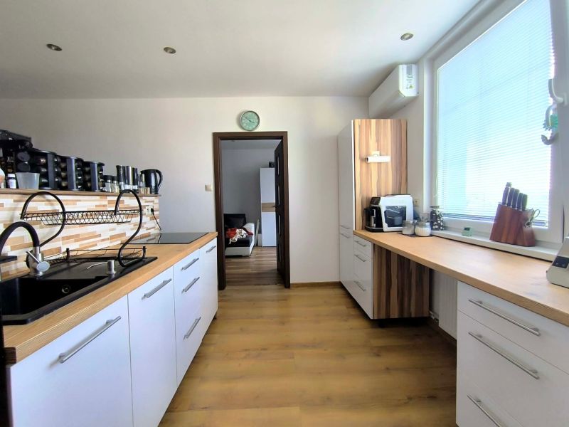 A kitchen in a 3-room apartment with a wooden decor floor and a large window.
