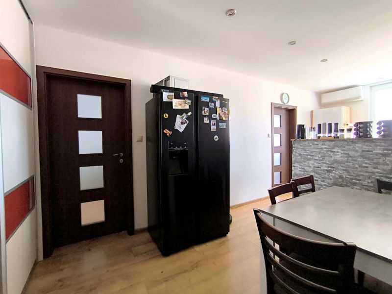 A kitchen in a 3-room apartment with a dining table, a black refrigerator, and a wooden decor floor.