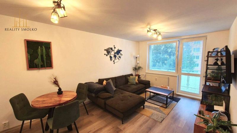 Living room in a three-room apartment with a wooden decor floor, a comfortable sofa, and a dining table.