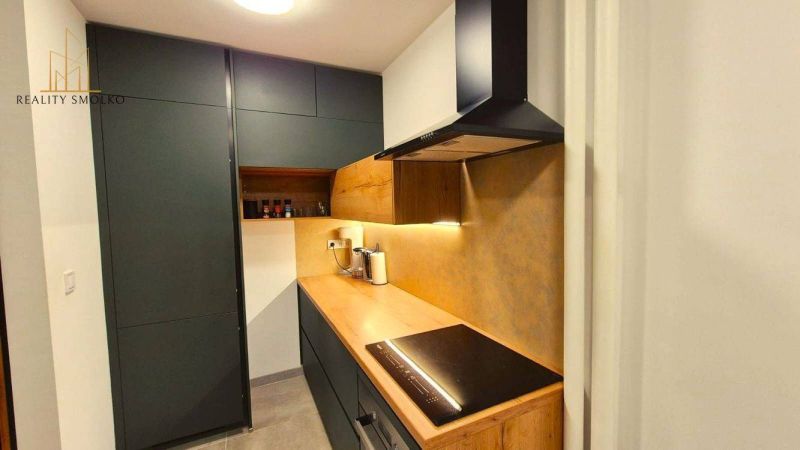 A kitchen in a 3-room apartment with a wooden decor floor and dark cabinets.
