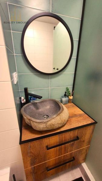 A bathroom in a 3-room apartment with a stone sink and a wooden decor floor.