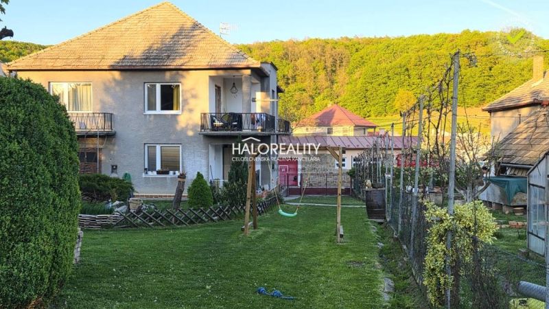 A family house in Poltár with a balcony, garden, and swing, surrounded by greenery.