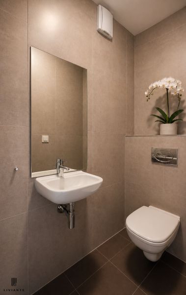 Bathroom with a sink, mirror, and toilet in a 3-room apartment with light-colored tiles.