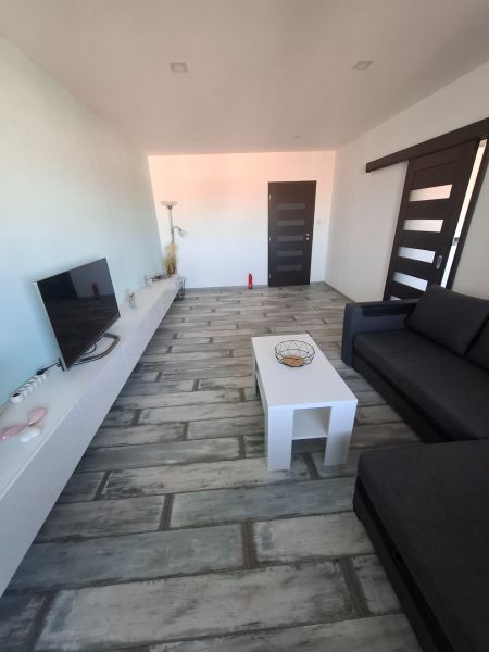 A living room with a black sofa, a white table, and a wooden decor floor in a three-room apartment.