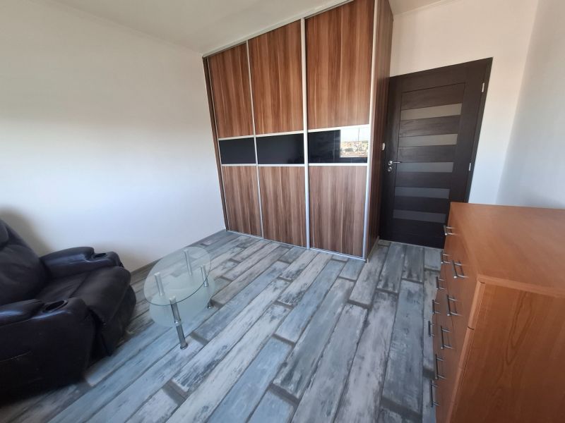 A room with a sofa, a wardrobe, a table, and a floor with a wooden decor in a 3-room apartment.