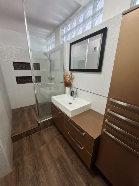 A bathroom with a shower, a mirror, and a wooden decor floor in a 3-room apartment.