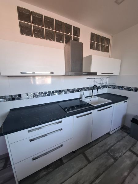 A kitchen in a 3-room apartment with glossy white cabinets and a dark countertop.
