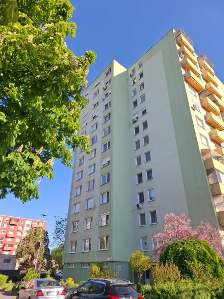 A view of the apartment building near B. Němcová in Nové Zámky, surrounded by greenery and cars.