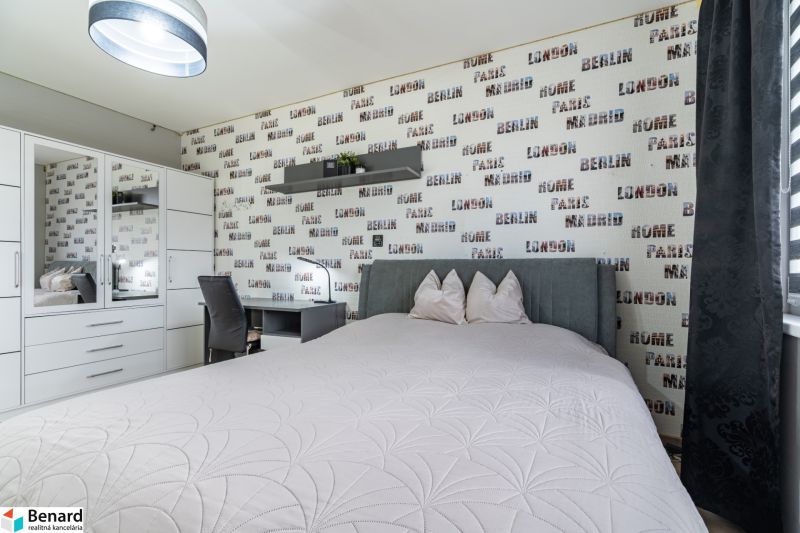 A bedroom with a feature wall with a pattern of inscriptions, next to a wardrobe and a desk.