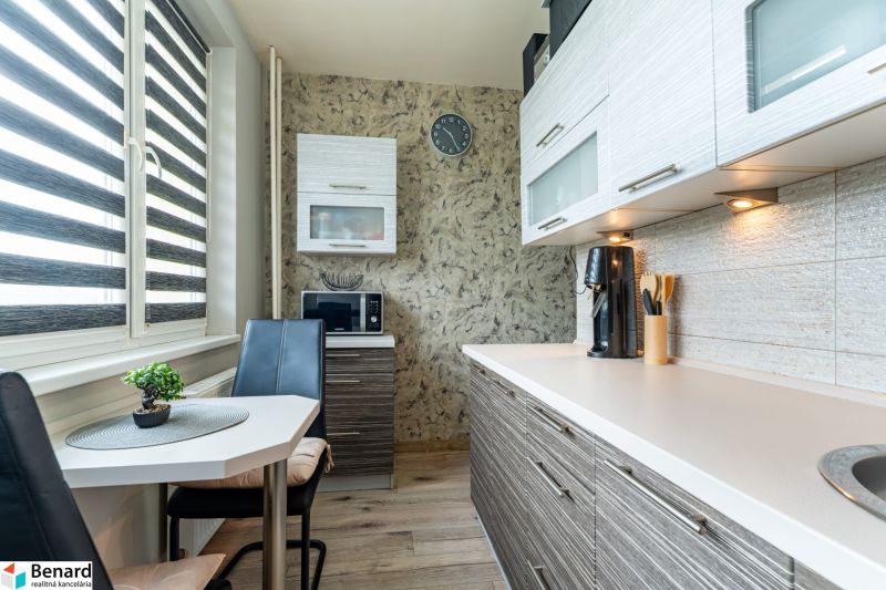 A kitchen in a 2-room apartment with a microwave, brown cabinets, and a table with chairs.