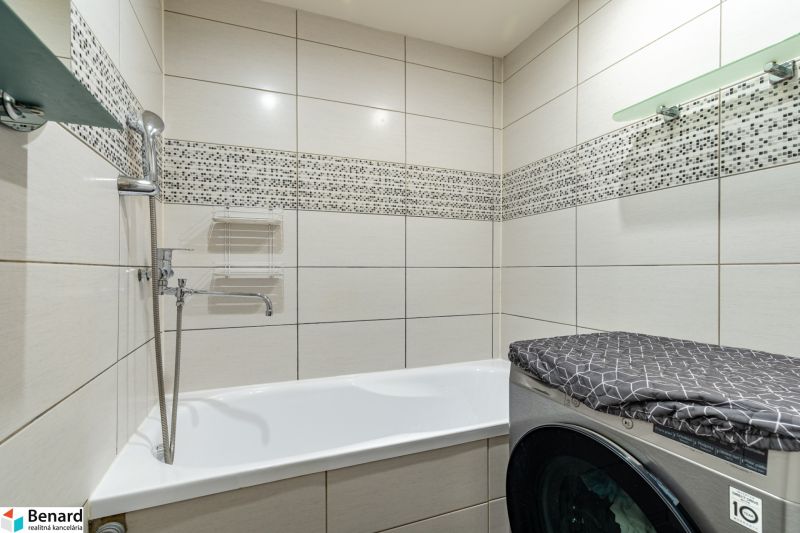A bathroom with a bathtub, a washing machine, and tiles in a 2-room apartment.