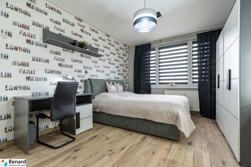 A bedroom in a two-room apartment with a bed, a desk, and a wooden decor floor.