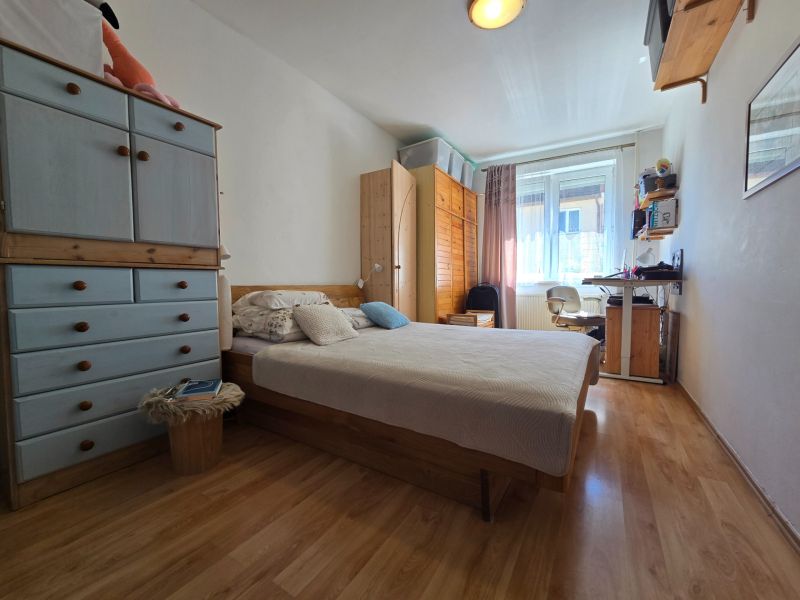 Bedroom in a two-room apartment with a wooden decor floor, a bed, and a work desk.