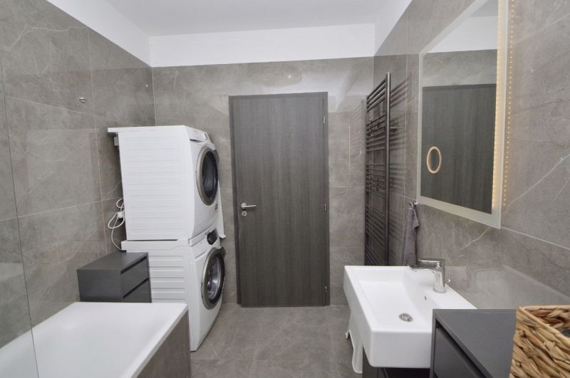 A bathroom in a family house with a washing machine, dryer, and bathtub, gray tiles.