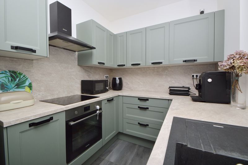 A kitchen in a family house with green cabinets and a marble countertop.