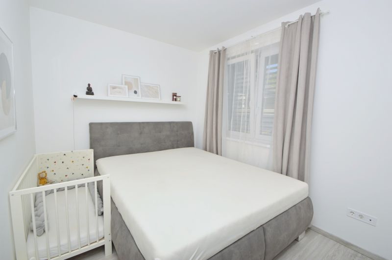 Bedroom in a family house with a double bed, a crib, and decorations on the shelf.