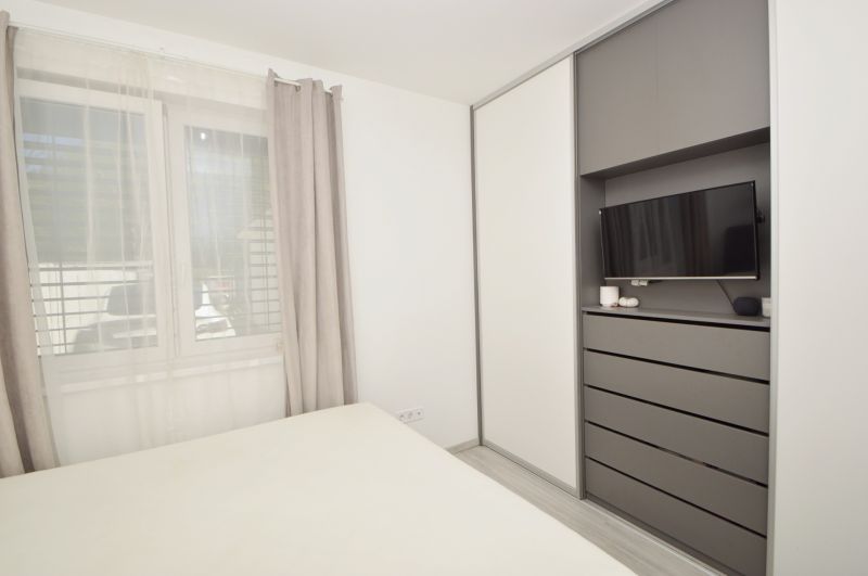 A bedroom in a family house with a television, a wardrobe, and a large window with curtains.