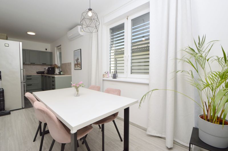 Dining room in a family house with a white table, pink chairs, and a green kitchen.