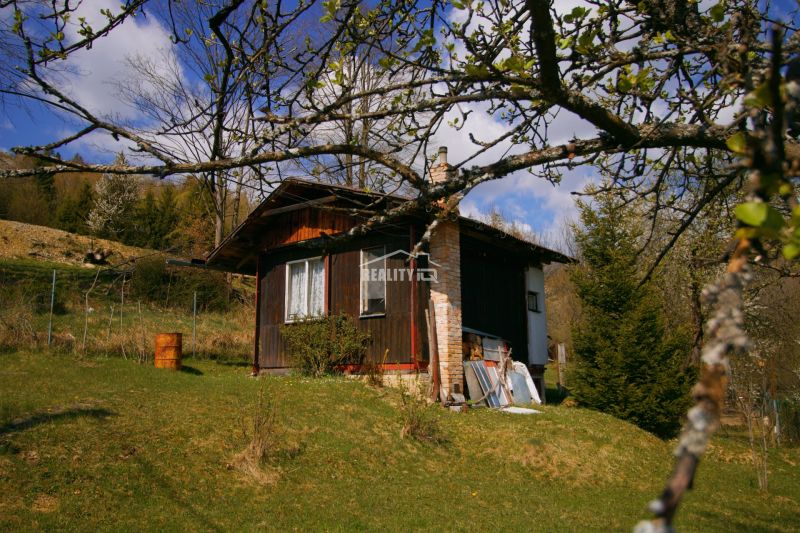 A wooden cottage in Krásno nad Kysucou surrounded by trees and grass on a slope.