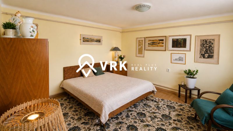 Bedroom in a family house with a blanket, wooden furniture, and artistic paintings on the wall.